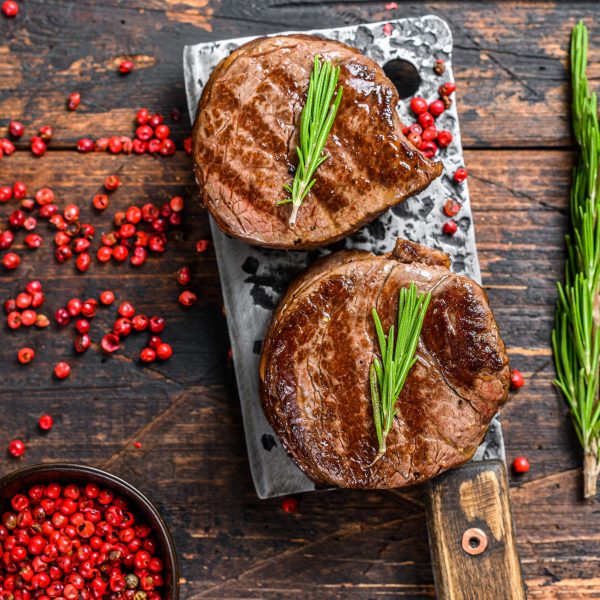 Grilled fillet mignon steak on a meat cleaver. Dark wooden background. Top view.