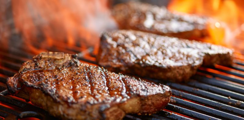 grilling steaks on flaming grill and shot with selective focus