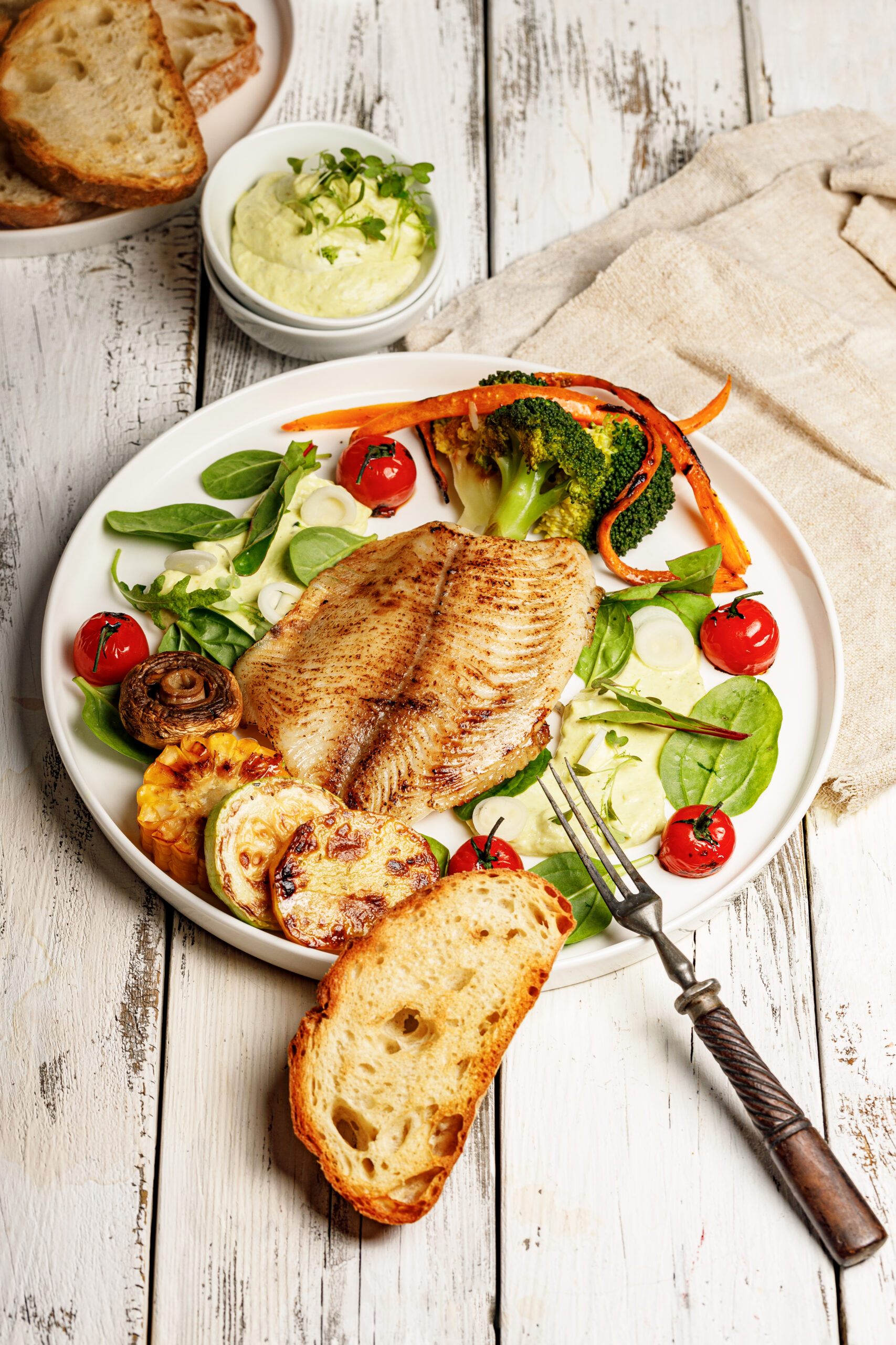 Fried sea fish and vegetables. Tilapia fillet with broccoli, cherry tomatoes and lettuce. Sea food on a white plate on white background. Vertical shot