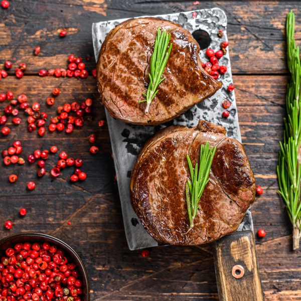 Grilled fillet mignon steak on a meat cleaver. Dark wooden background. Top view.